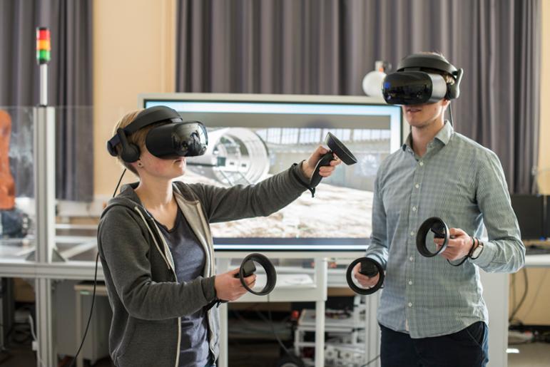 Mann und Frau mit VR-Datenbrillen und Controllern vor Bildschirm mit Computer-Animation