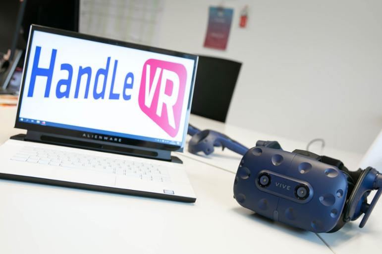 Aufgeklappter Laptop mit Logo HandLeVR auf Bildschirm. Daneben liegt VR-Datenbrille
